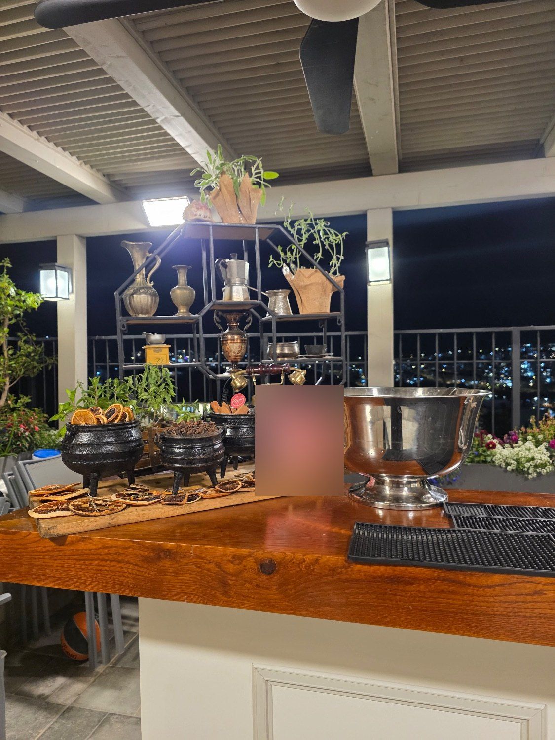 סירי תבלינים ופרוסות תפוז על בר עץ, עם נוף לילי של העיר