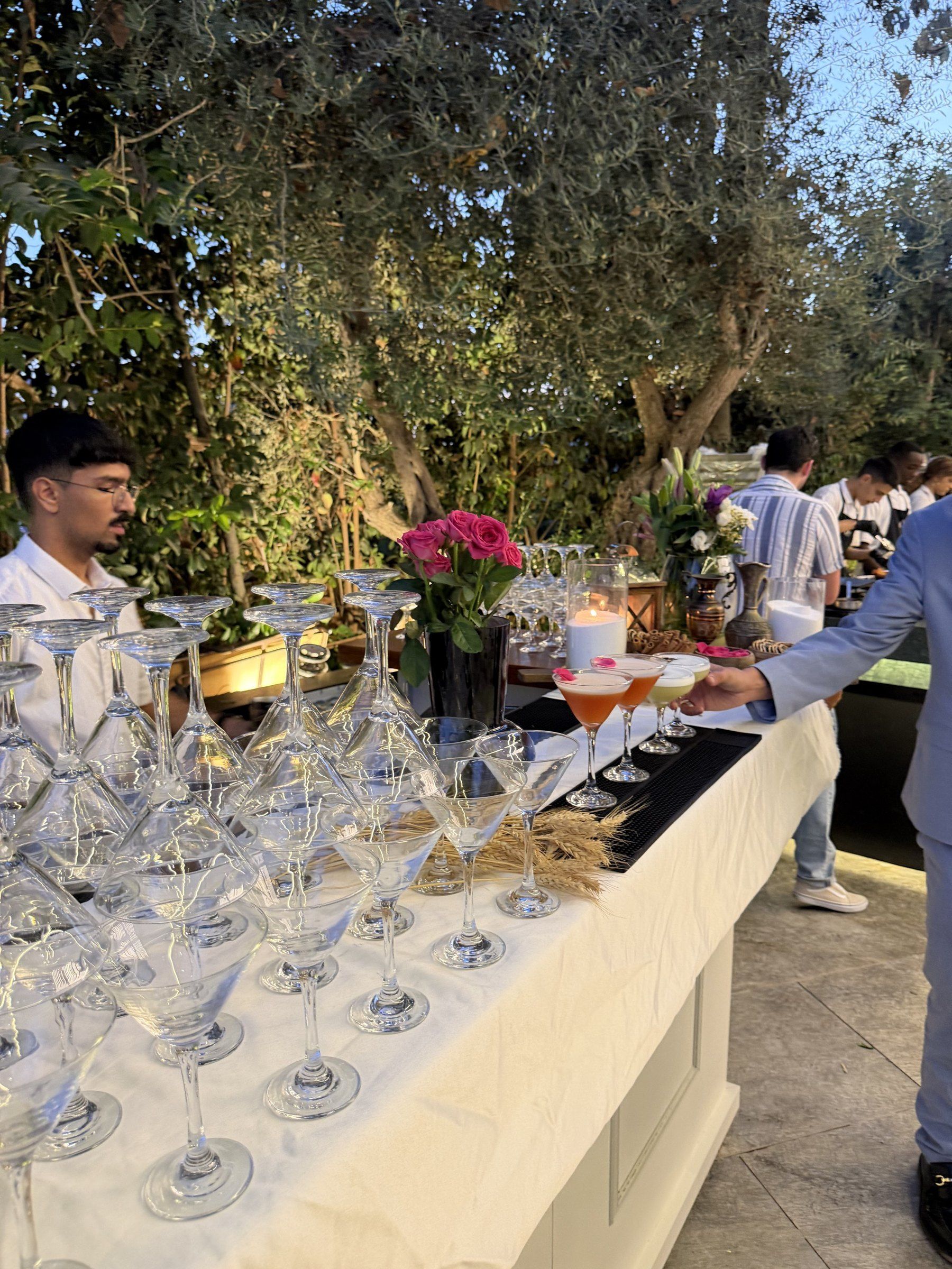 ברמן מגיש קוקטיילים לאורחים בבר בגינה עם כוסות מרטיני