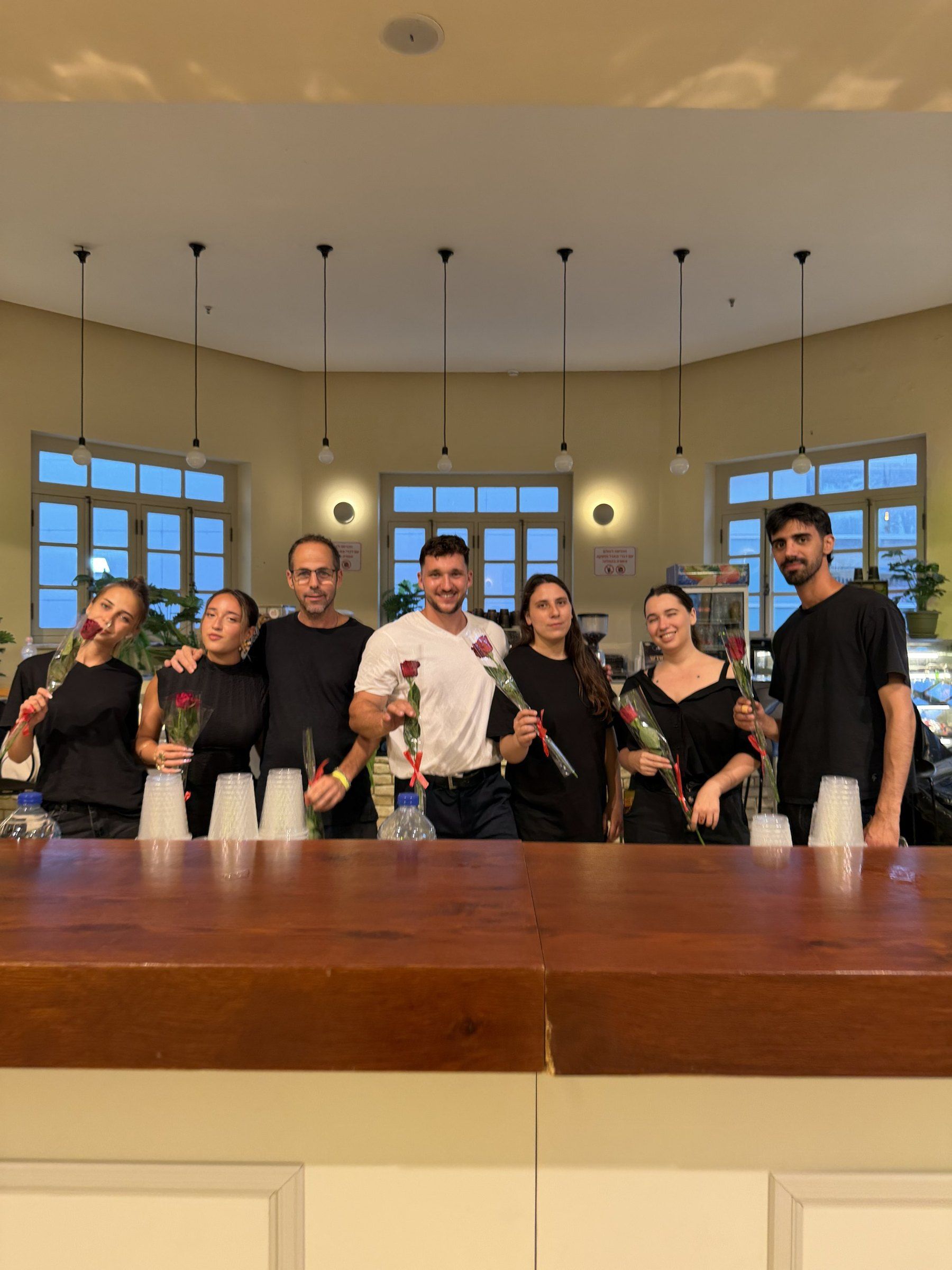 צוות Prime Bar עומד מאחורי הבר, כל אחד עם ורד ביד